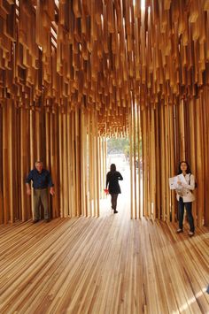 two people are walking through a bamboo room with wooden columns on the walls and wood flooring