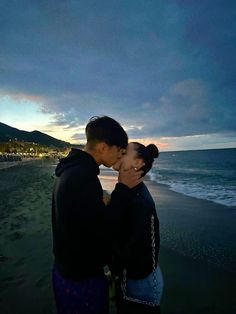 two people are kissing on the beach at night time, while the sun is low in the sky