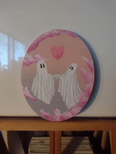 two white ghostes in front of a pink background on a wooden shelf with paper hearts