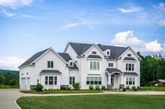 a large white house sitting in the middle of a lush green field on a sunny day