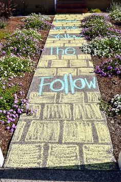 the sidewalk has words written on it and flowers in front of a house that says follow