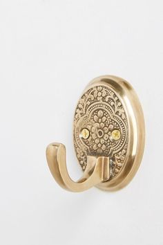 an ornately designed brass hook on a white wall with a gold colored handle and decorative design