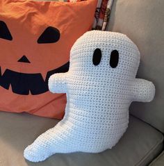 a crocheted ghost pillow sitting on top of a couch next to a pumpkin pillow