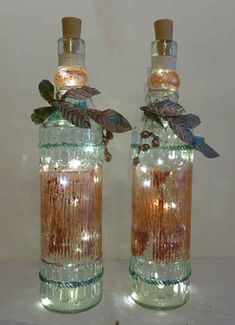 two glass bottles with leaves on them sitting next to each other