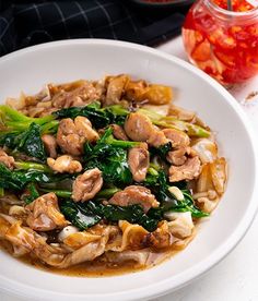 a white bowl filled with noodles and vegetables on top of a table next to a jar of seasoning