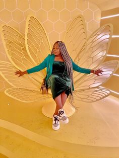 a woman in a green dress sitting on top of a butterfly shaped chair with her arms outstretched