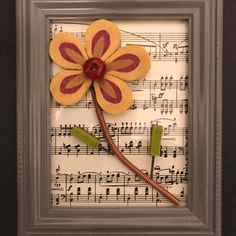 a piece of art made out of sheet music with a flower and two sticks sticking out of it