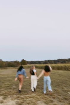 three women are running in a field holding hands