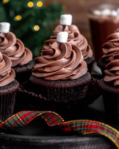 cupcakes with chocolate frosting and marshmallows on top, next to a christmas tree