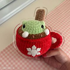 a hand is holding a small crocheted cup with a stuffed animal in it