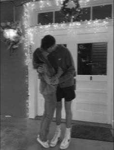 black and white photograph of two people kissing in front of a house with christmas lights