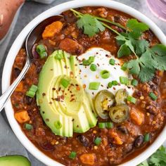 a white bowl filled with chili, beans and avocado on top of a table