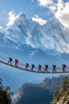 a group of people walking across a suspension bridge in front of a snow covered mountain