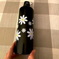 a hand holding a black water bottle with white daisies on it