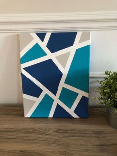 a blue and white painting sitting on top of a wooden table next to a potted plant