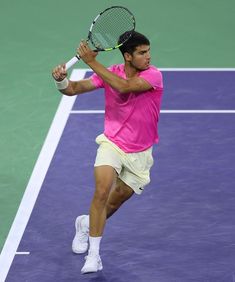 a male tennis player in a pink shirt and white shorts is swinging his racket