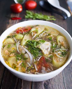 a white bowl filled with vegetable soup on top of a wooden table next to tomatoes