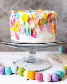 a cake with white frosting and multicolored icing on a glass platter