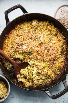 a large skillet filled with some food on top of a blue counter next to two bowls