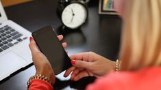 a woman sitting at a desk looking at her cell phone while holding it in her hand