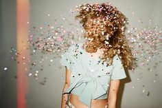 a woman standing in front of a wall with confetti falling from her hair