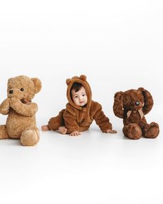 three stuffed animals sitting next to each other in front of a white background with a baby wearing a teddy bear costume