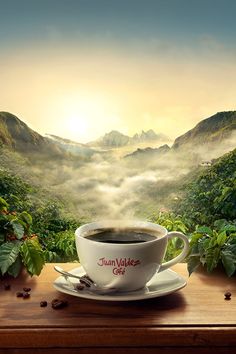 a cup of coffee sitting on top of a wooden table next to a mountain range