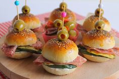 mini sandwiches with olives and ham are on a wooden platter topped with toothpicks