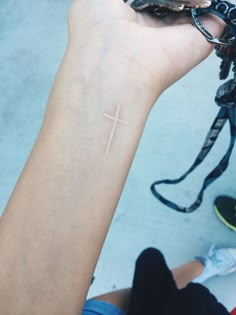 a person with a small cross tattoo on their left wrist, holding a cell phone