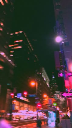 a city street at night with traffic lights and people walking on the sidewalk in the foreground