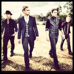 three men in suits and hats are walking down the dirt road with trees in the background