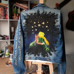 a denim jacket with the image of tinkerbell sitting on top of a wooden easel