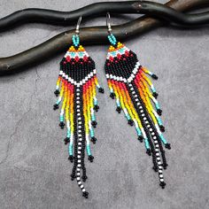 Make a bold statement with these extra long beaded shoulder dusters. Designed in rich native colors, these earrings feature a striking black chevron motif adorned with vibrant accents in red, blue, orange, and yellow. The eye-catching long fringe showcases a dynamic combination of bright colors, with a bold black-and-white striped section in the center for added contrast. Perfect for boho, tribal, and ethnic fashion lovers, these earrings add a touch of cultural elegance to any outfit. Lightweig Bohemian Multicolor Beaded Earrings With Black Beads, Multicolor Traditional Beaded Earrings, Bohemian Multicolor Long Drop Beaded Earrings, Southwestern Black Beaded Earrings For Festivals, Multicolor Long Drop Jewelry For Festivals, Artisan Fashion, Long Fringe, Writing Gifts, Black Chevron