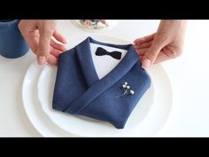 two hands are holding a blue jacket and bow tie on a white plate next to another person's hand