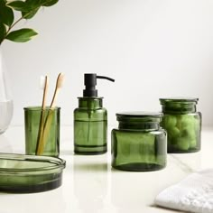 green glass containers with toothbrushes and soap dispensers on a counter