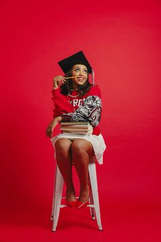 a woman sitting on top of a white stool wearing a graduation hat and holding books