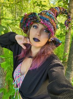 a woman with pink hair wearing a knitted hat and black sweater in the woods