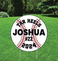 a baseball shaped yard sign on top of a green grass covered field with trees in the background