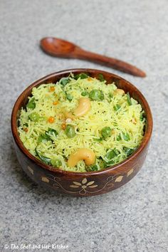 a wooden bowl filled with rice and vegetables next to a spoon on the ground in front of it