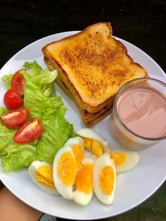 a white plate topped with an egg, toast and salad next to a cup of juice