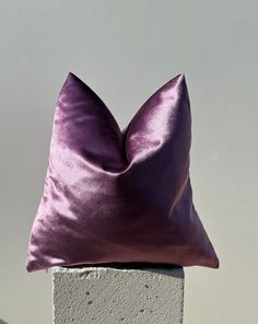 a purple pillow sitting on top of a cement block in front of a white wall