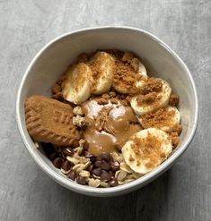 a white bowl filled with cereal and banana slices on top of chocolate chips, peanut butter and graham crackers