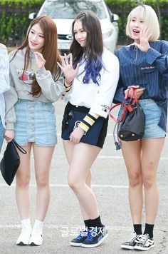 three girls are standing in a parking lot and one girl is making the peace sign