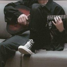 a man sitting on top of a couch holding a guitar next to his feet and playing the guitar