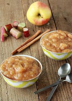 two bowls filled with apples and cinnamon on top of a wooden table next to spoons