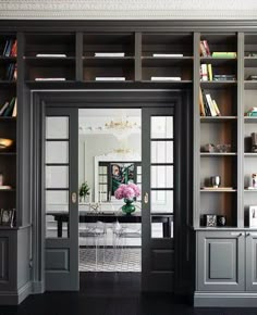 an open door leading to a dining room with built - in bookshelves and chairs