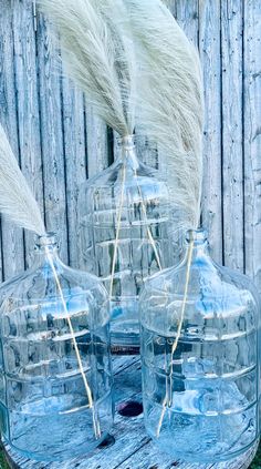 three clear glass vases with white feathers in them sitting on a wooden table next to a fence