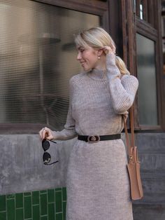 a woman is walking down the street with her hand on her hip and wearing a gray sweater dress