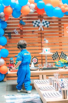 a young boy standing in front of a table with balloons and cake on top of it