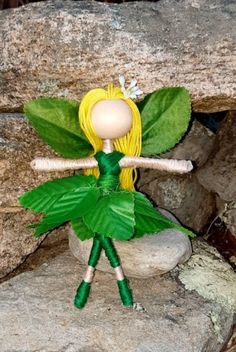 a green fairy doll sitting on top of a rock next to some leaves and rocks